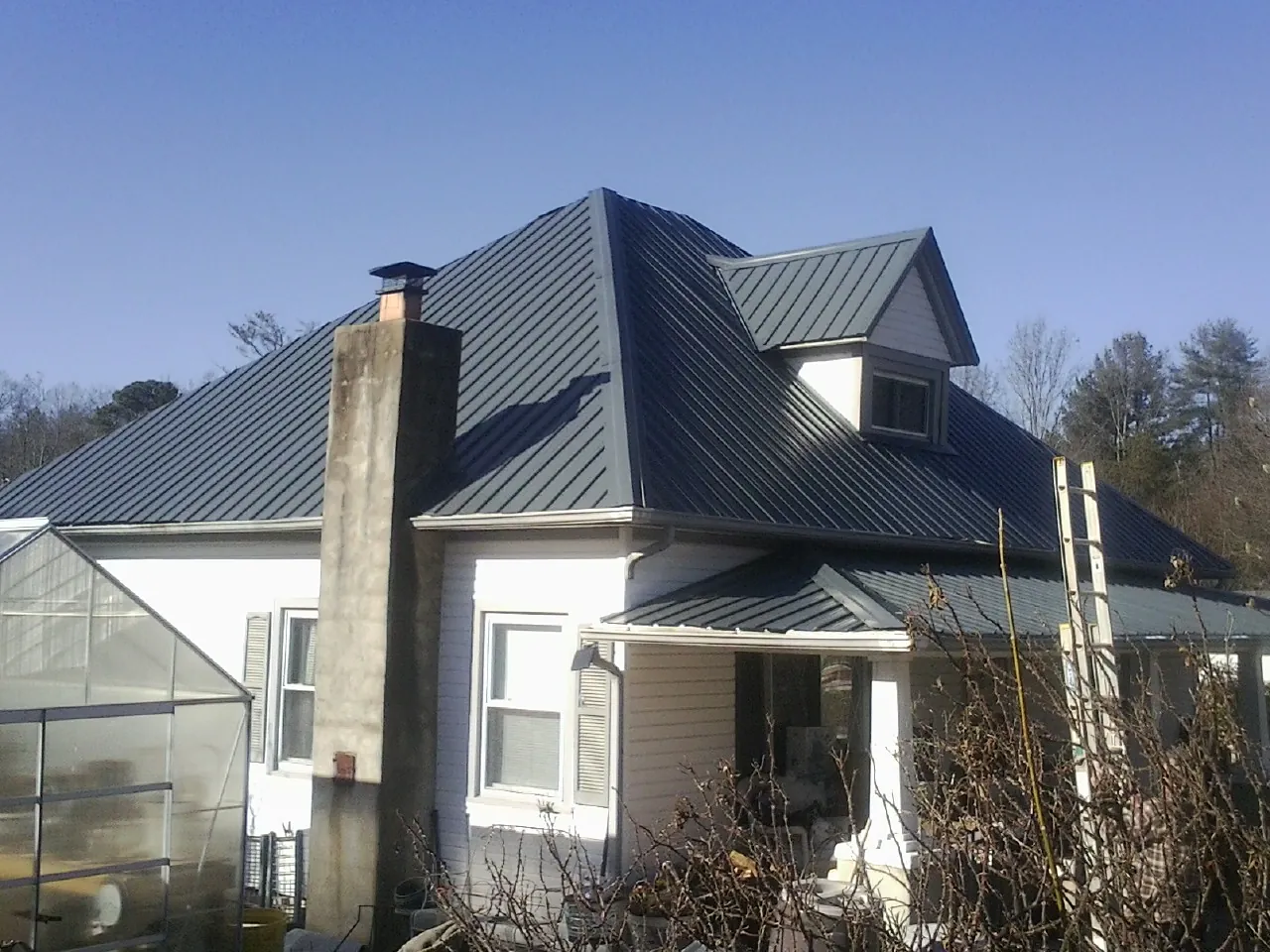 Dark blue standing seam metal roof on a white farmhouse with dormer — Slate & Tile Roof Repair by Roofing Brothers in West Alton