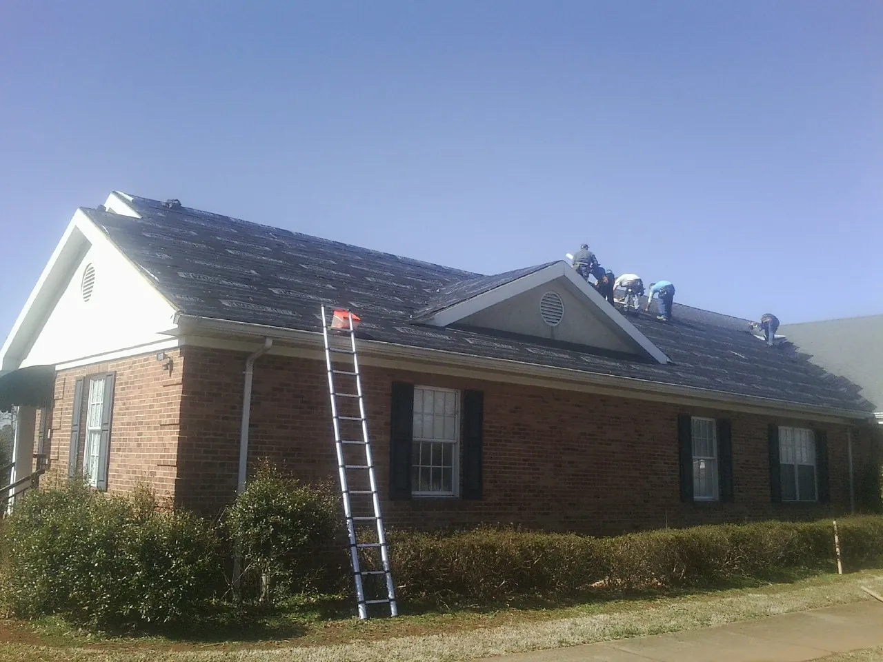Crew tearing shingles off a brick ranch roof with a ladder set — Emergency Roof Repair work by our crew in West Alton