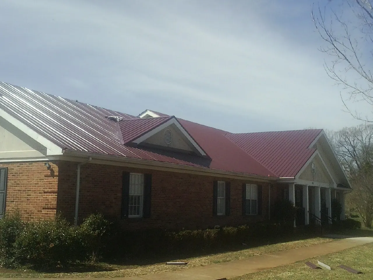 Red metal roof with gabled entries on a long brick building, from a Hail Damage Roof Repair job in West Alton