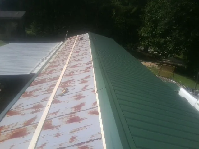 Old rusted panels beside newly installed green metal roofing — Wind Damage Roof Repair by Roofing Brothers in West Alton