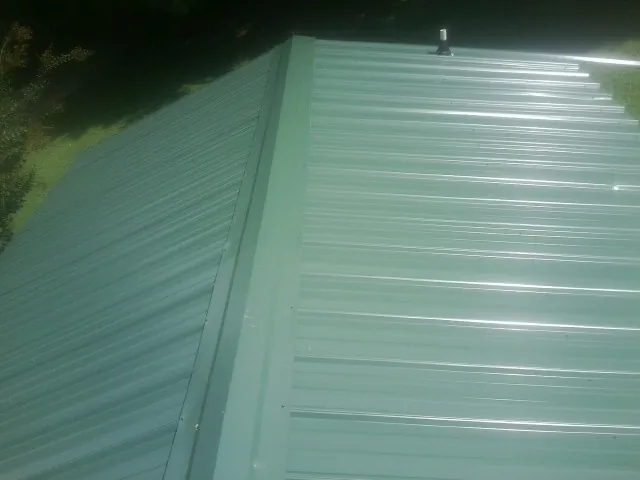 New green metal panels meeting at the ridge of a roof — Flat Roof Repair work by our crew in West Alton