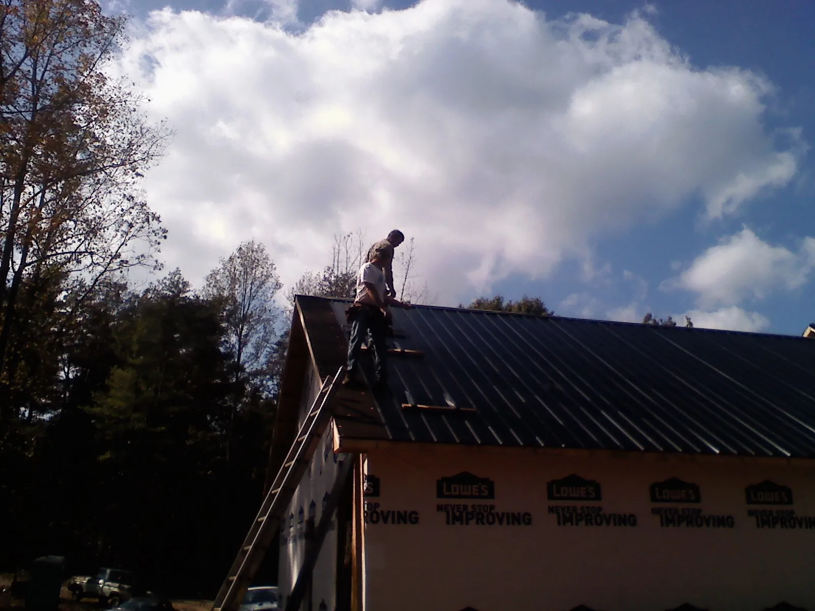 Roofer fastening dark metal panels high against a cloudy sky, from a Roof Inspection job in West Alton