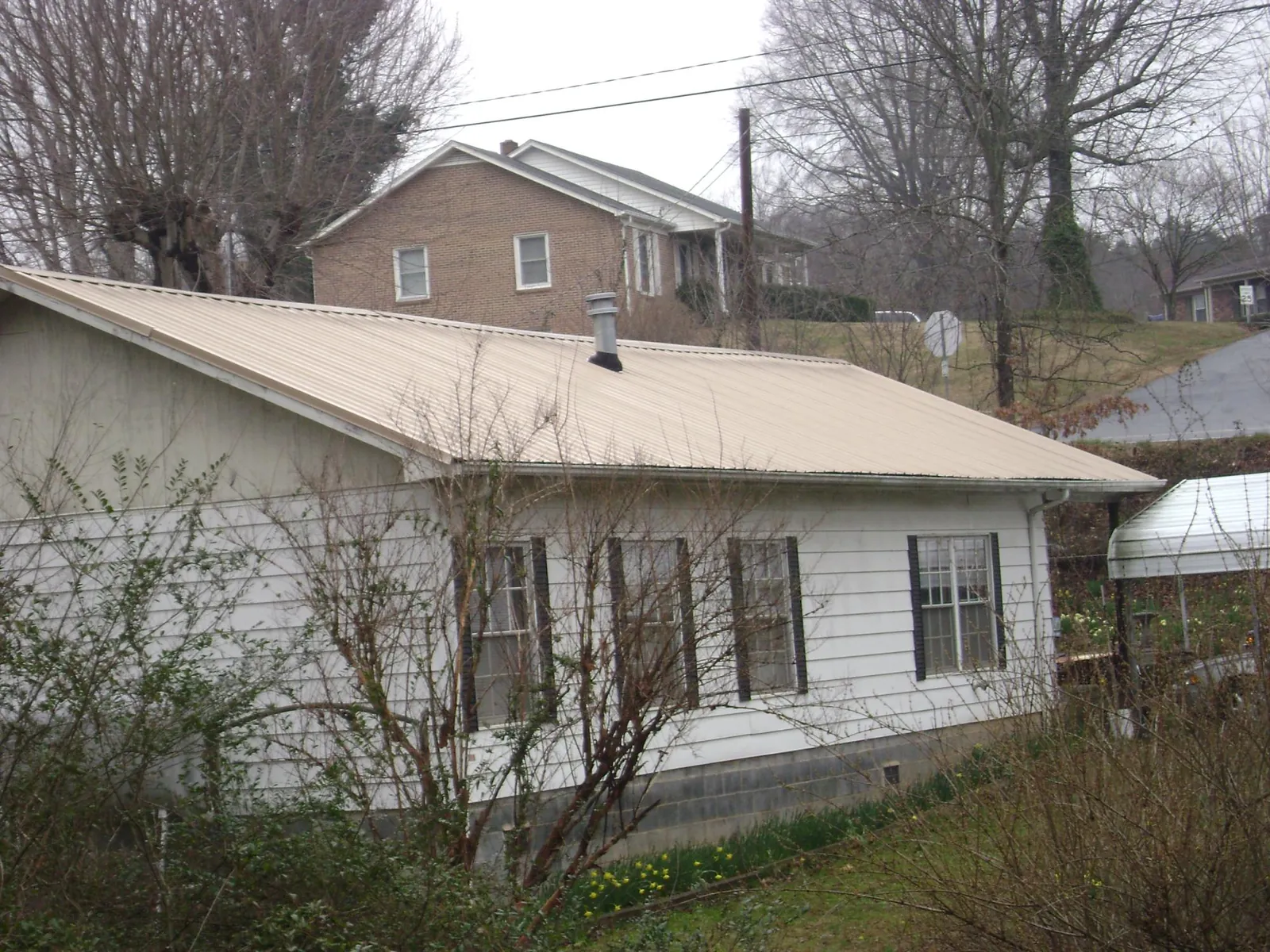 Tan metal roof on a white sided house set into a hillside — Commercial Roofing by Roofing Brothers in West Alton