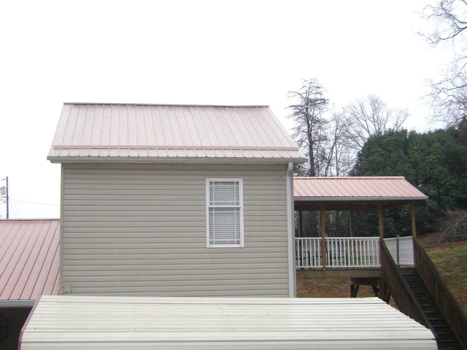 Tan metal roofs on a two story addition and attached porch, from a Roof Replacement job in West Alton